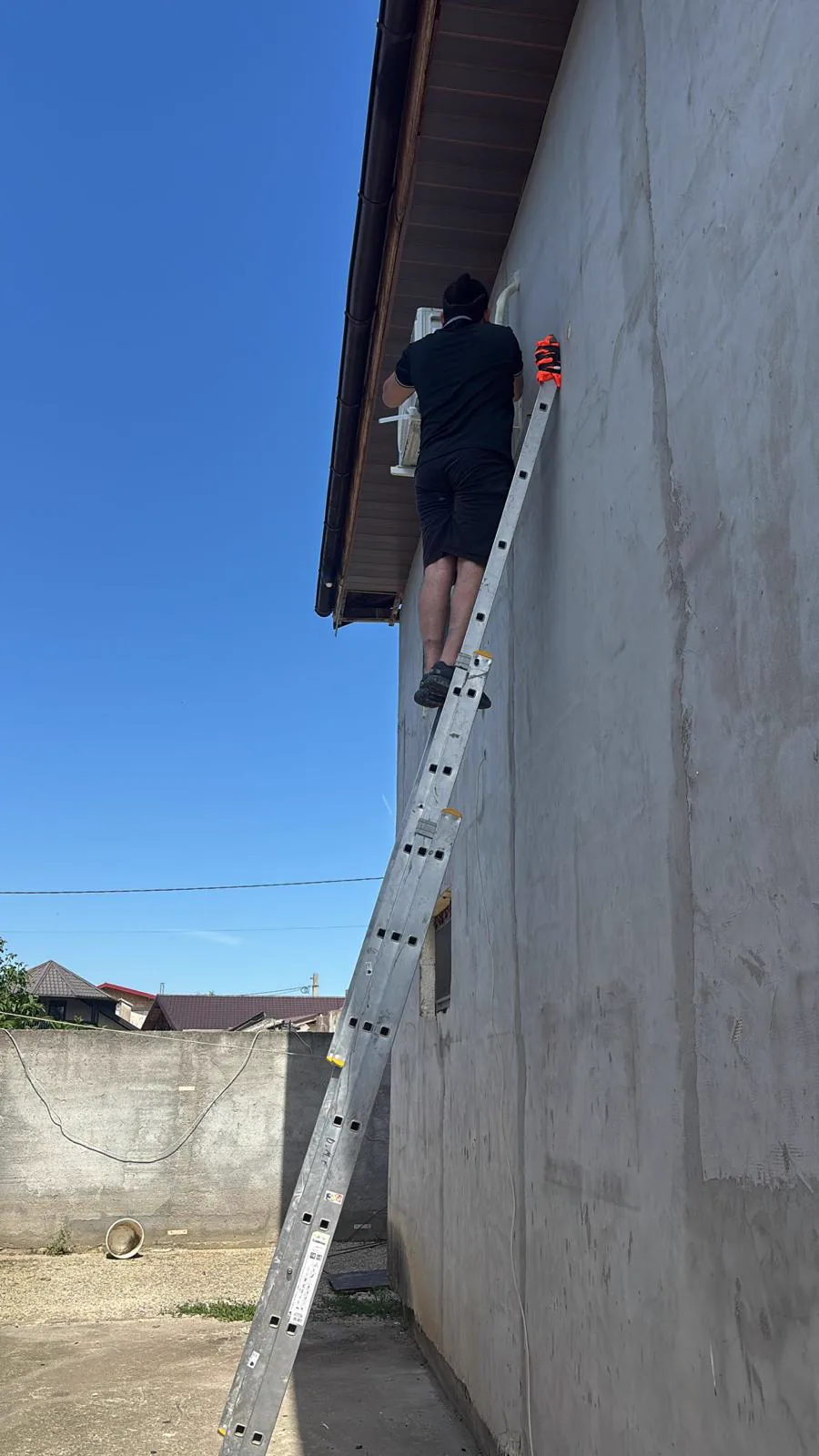 Tehnician pe scara la montajul unei unitati exterioare de aer conditionat la casa